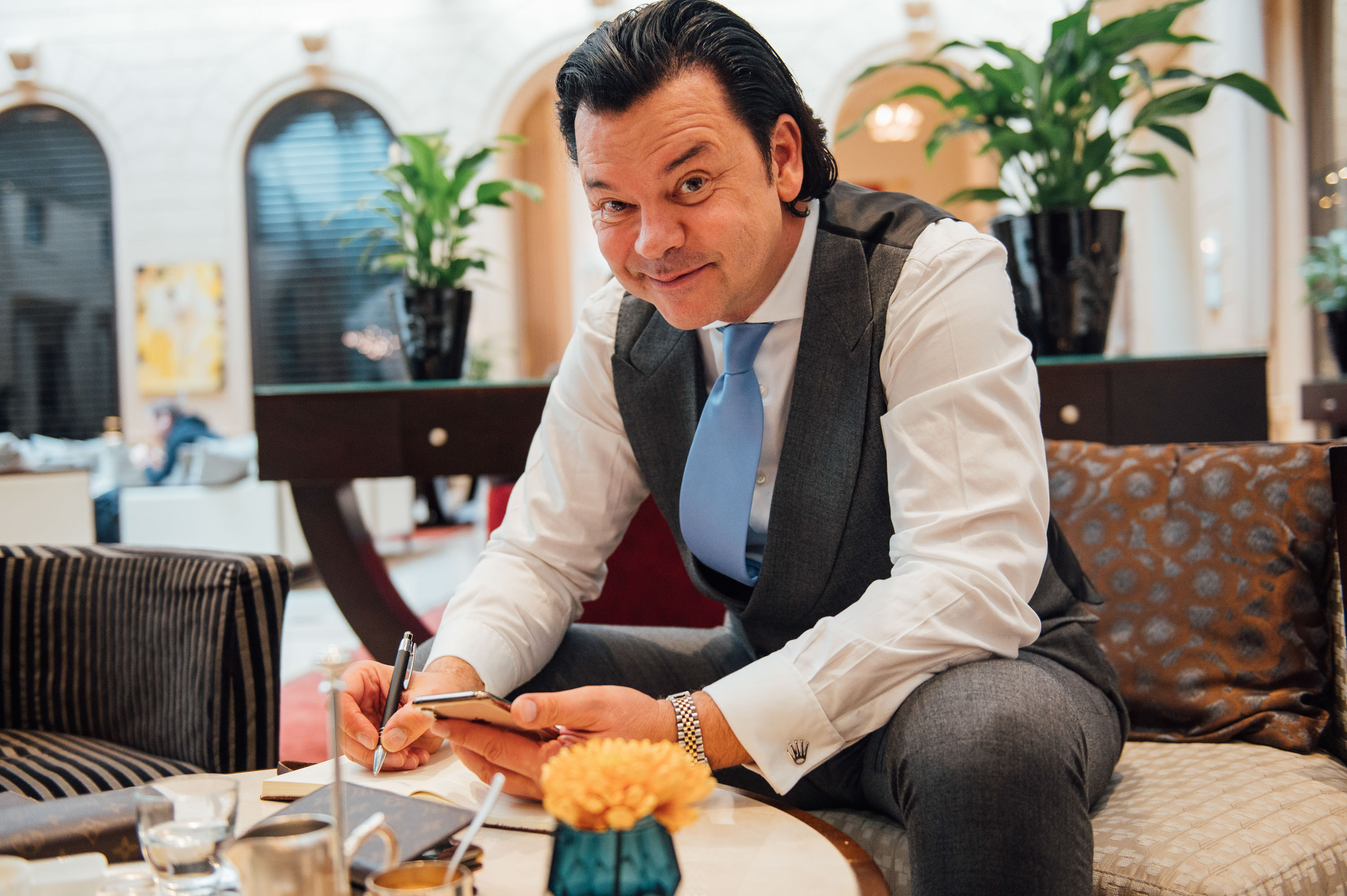 Finanzt- und Immobilientrainer im Anzug mit Smartphone und Stift in einer Hotellobby